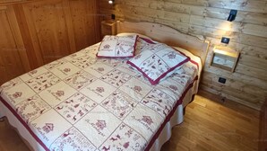 Een slaapkamer met een houten schuine plafond, een bed met een beddegoed met een patroon, en twee wandlampen.