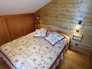 Een slaapkamer met een houten schuine plafond, een bed met een beddegoed met een patroon, en twee wandlampen.