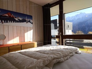 Ein Schlafzimmer mit einem großen Bett, einem Holzkopfende, einem Nachttisch, einem Spiegel und einem Fenster mit Blick auf die Berge.