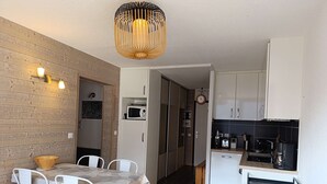 A compact kitchen with white cabinets, a microwave, and a coffee machine. There is a dining area with a table and chairs, and a sofa in the corner.