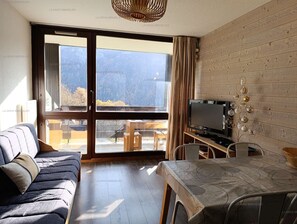 Un saló modern amb un sofà, una taula de dinar, una televisió i vista a un paisatge de muntanyes.