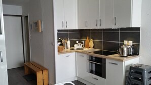 A compact kitchen with white cabinets, a black tiled backsplash, a sink, a stove, and a small wooden bench.