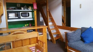 A compact living space with a kitchenette, a wooden staircase, and a sofa with a blue pillow. - Paradiski closed to the slopes vallandry (LANDRY)