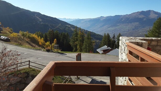 A mountain view from a wooden deck with a stone wall and a road in the foreground. - Paradiski closed to the slopes vallandry (LANDRY)
