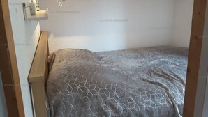 A small bedroom with a bed, a nightstand, and wooden cabinets above.