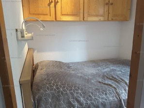 A small bedroom with a bed, a nightstand, and wooden cabinets above.