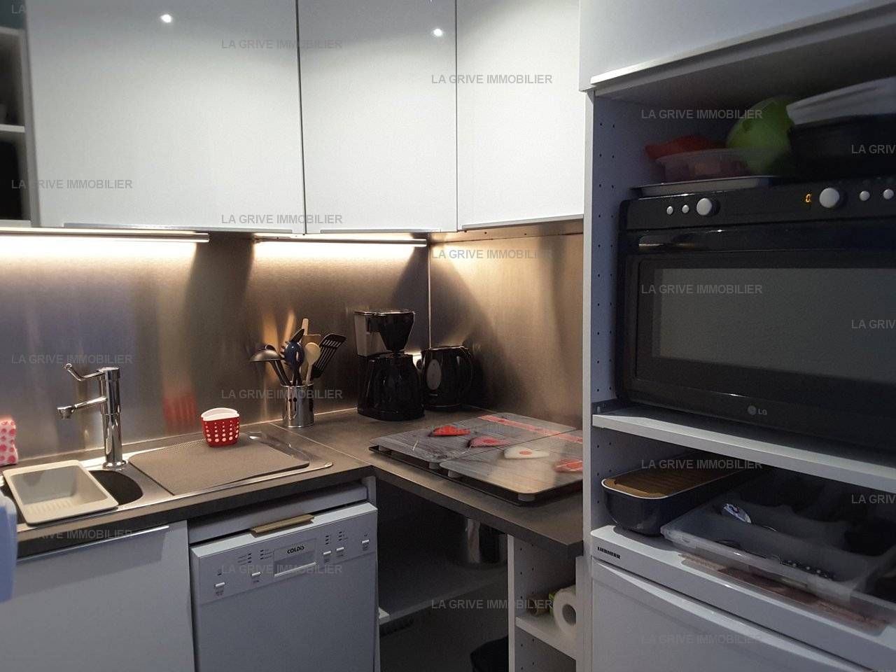 A modern kitchen with a dishwasher, coffee maker, and a flat-screen TV.