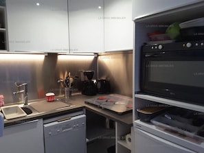 A modern kitchen with a dishwasher, coffee maker, and a flat-screen TV.