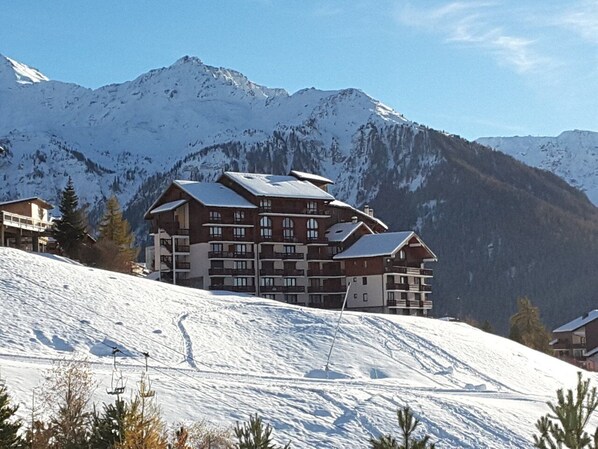 A multi-story hotel with a ski slope in the foreground, surrounded by snow-covered mountains.