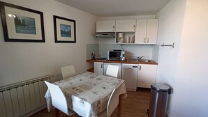 Een compacte kitchenette met een magnetron, fornuis en spoelbak. Er staat een tafel met stoelen en eronder een radiator.