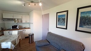 Een compacte leefruimte met een kitchenette, een eethoek en een zithoek met een bank.
