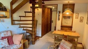 Ein gemütliches Wohnzimmer mit einer Holztreppe, einem Esstisch und einem Korbstuhl.