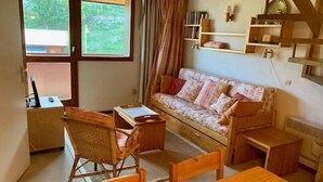 Ein gemütliches Zimmer mit einem Holztisch, einem blumigen Sofa, einem Korbstuhl und einem Schreibtisch mit einem Computer.