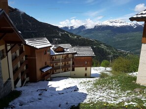 Un chalet avec une façade en bois, un balcon et une vue sur des montagnes enneigées.