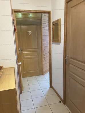 A hallway with a wooden door, a small framed picture, and a tiled floor.