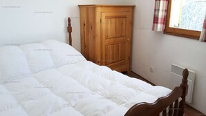 Une chambre avec une armoire en bois, un lit avec une literie blanche et une fenêtre donnant sur des arbres.