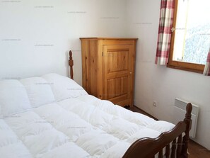 Une chambre avec une armoire en bois, un lit avec une literie blanche et une fenêtre donnant sur des arbres.