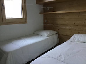 Une chambre avec deux lits simples, une fenêtre et un lambris en bois sur le mur.