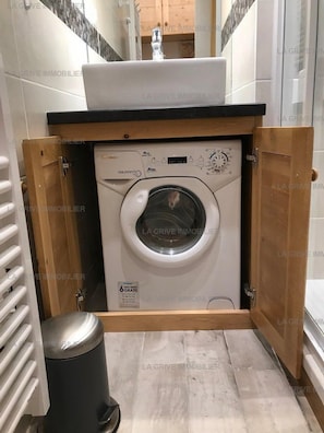 Un lave-linge compact, encastré, à chargement frontal, situé dans un petit espace clos doté d’une structure en bois.