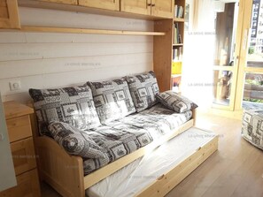 A wooden sofa with patterned cushions in a room with wooden flooring and a window.