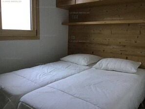 A bedroom with a wooden headboard, two beds with white bedding, and a window.