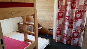 Un lit superposé avec un matelas rose, un petit tabouret, un panier et un rideau orné de motifs en forme de cœur.