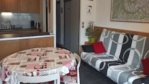 Un espace de vie compact comprenant un coin cuisine, une table à manger recouverte d’une nappe à motifs, un canapé avec des coussins à rayures et une grande carte accrochée au mur.