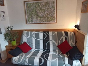 Une chambre avec un lit, une carte accrochée au mur, une plante en pot et une table de chevet.