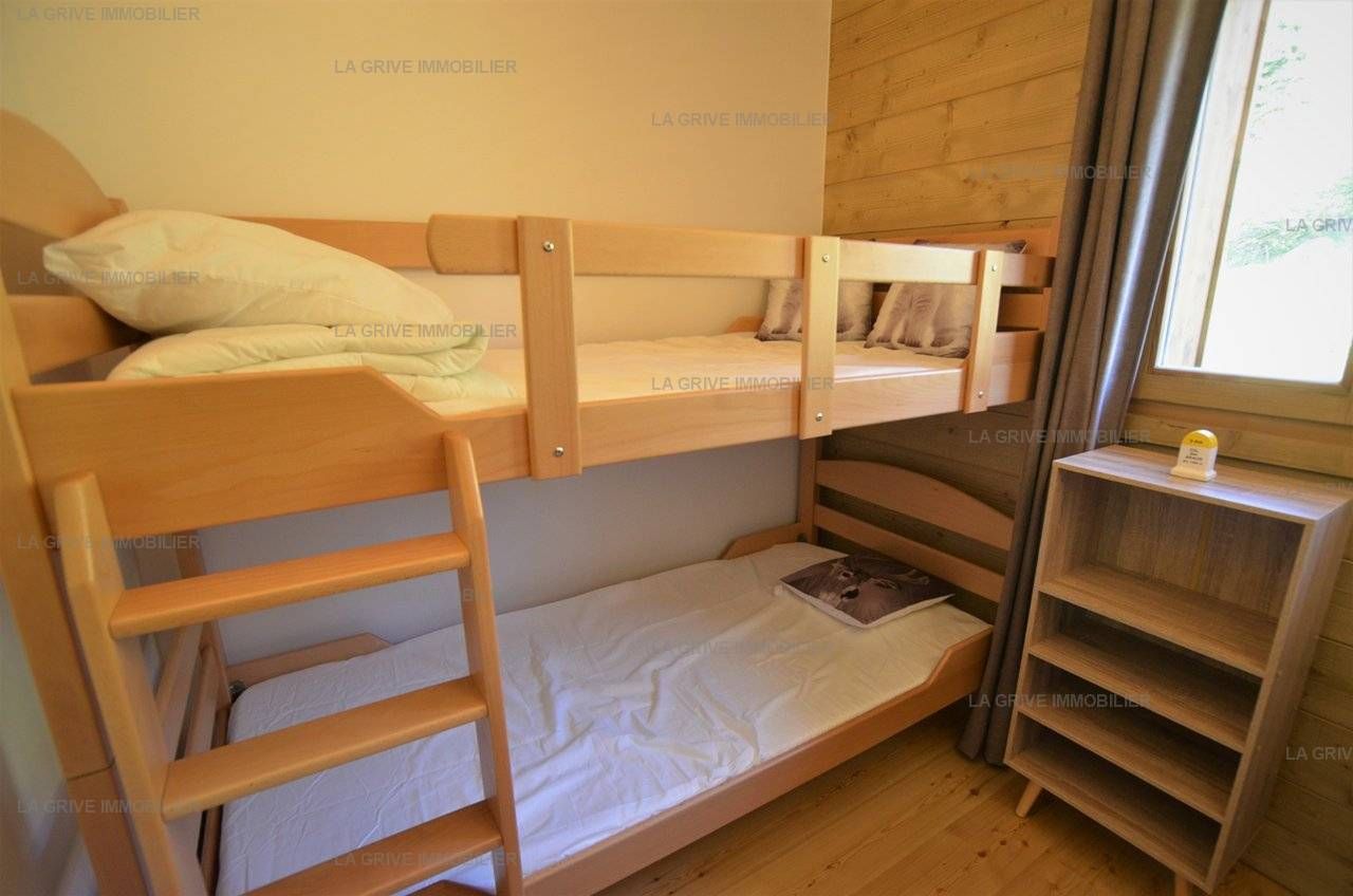 A bunk bed with a wooden ladder and a small shelf unit beside it.