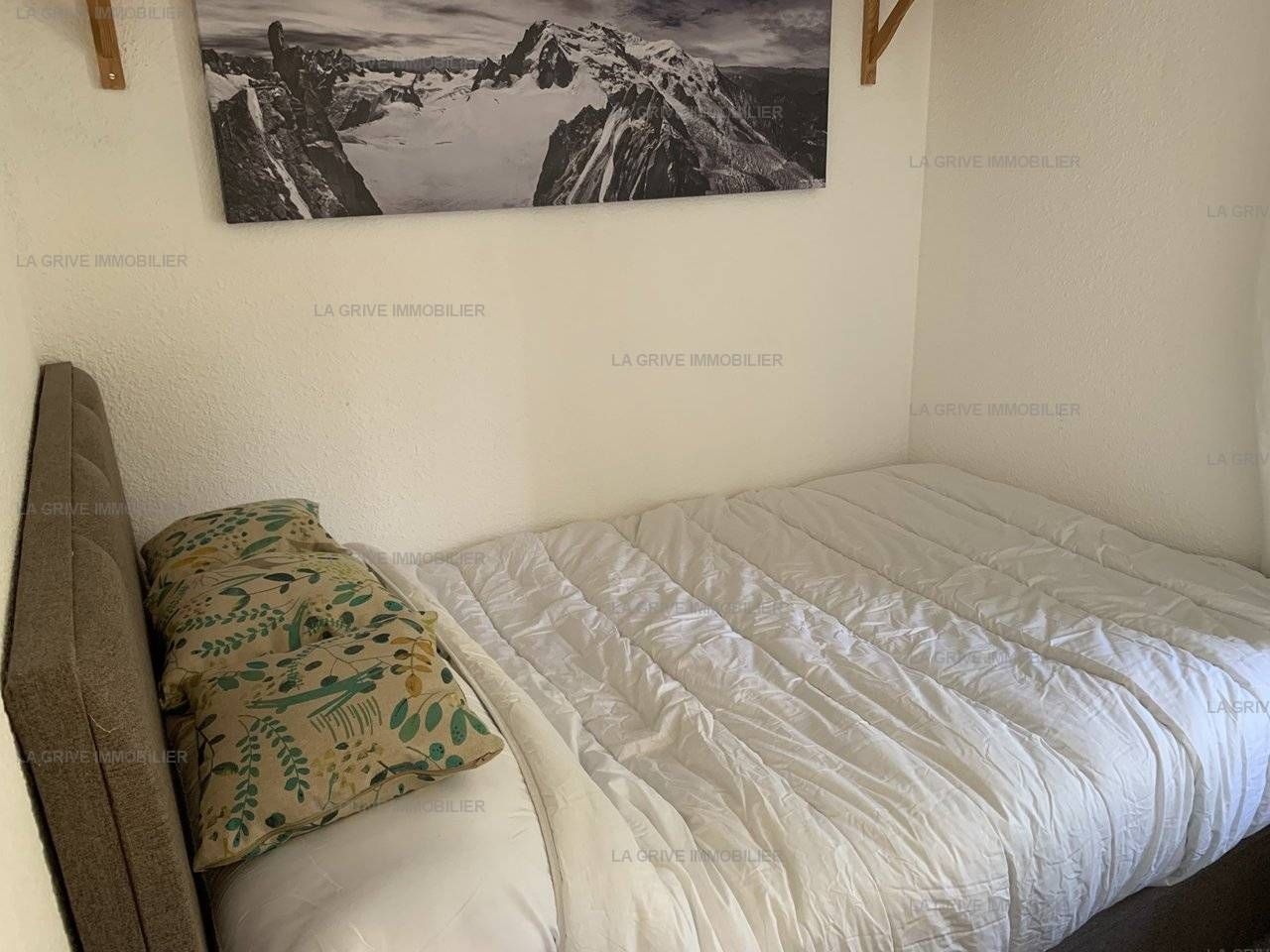 A bedroom with a bed, pillows, a headboard, and a framed picture on the wall.