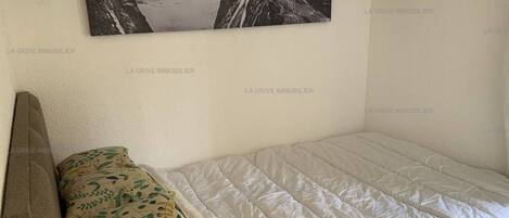 A bedroom with a bed, pillows, a headboard, and a framed picture on the wall.