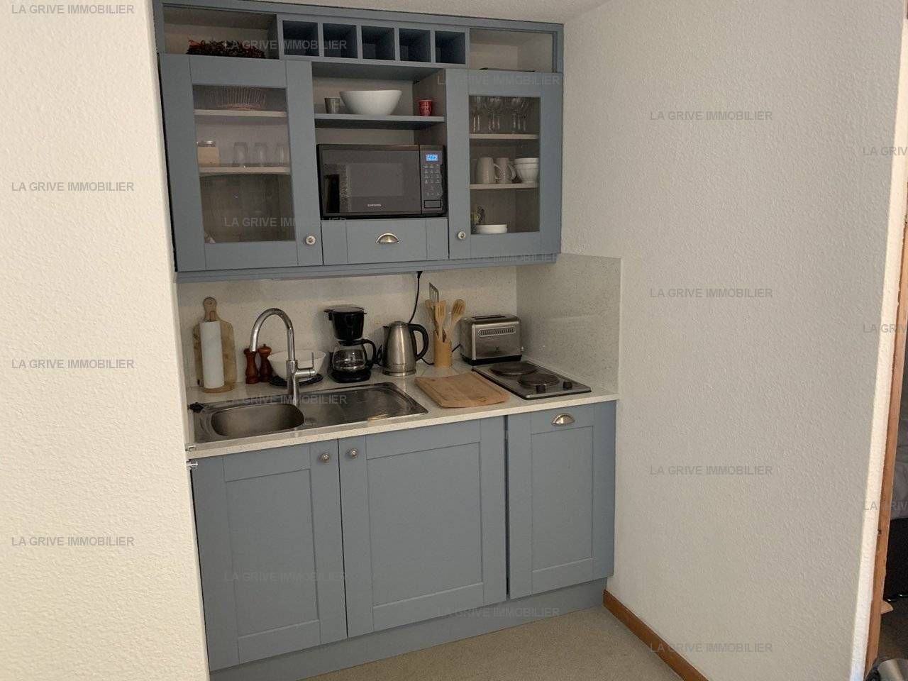 A compact kitchen with grey cabinets, a microwave, a coffee maker, and a toaster.