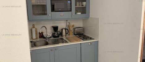 A compact kitchen with grey cabinets, a microwave, a coffee maker, and a toaster.