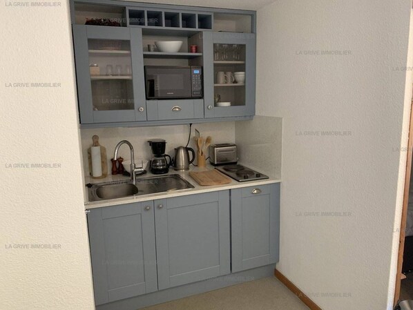 A compact kitchen with grey cabinets, a microwave, a coffee maker, and a toaster.