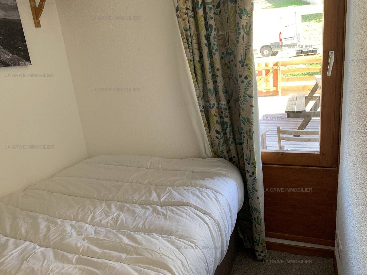 A bedroom with a bed, a wooden door, and a view of the outside.