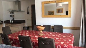 Un coin repas avec une nappe rouge, des chaises noires et un miroir encadré en bois accroché au mur.