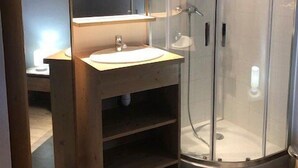 Une salle de bain moderne avec une douche à parois de verre, un meuble-lavabo en bois avec un miroir et un luminaire placé au-dessus du miroir.