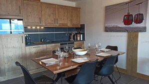 A modern kitchen with wooden cabinets, a dining table set for four, and a painting of a cable car on the wall.