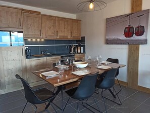 A modern kitchen with wooden cabinets, a dining table set for four, and a painting of a cable car on the wall.