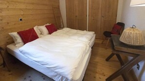 Ett rum med träpanel på väggarna, innehållande en säng, en stol, ett bord och en lampa.