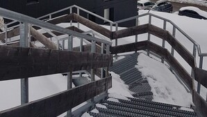 Ein modernes Gebäude mit dunkler Fassade und zahlreichen Fenstern, umgeben von verschneiter Landschaft und einer Bergkulisse.