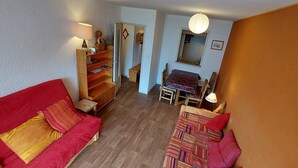 Ein kompakter Wohnraum mit einem roten Sofa, einem kleinen Esstisch und einer Holzkabine.