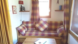 A cozy room with a plaid sofa, a small table, and a window with curtains.
