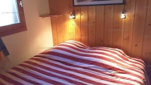 A room with a wooden paneled wall, a bed with a striped blanket, and a painting above the bed.