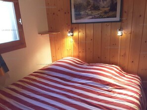 Una habitación con un revestimiento de madera, una cama con manta a rayas y un cuadro sobre la cama.