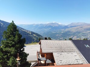 A mountain lodge with a view of distant mountains, a wooden deck, and a solar panel roof.