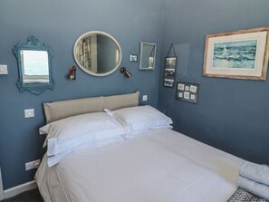 A bedroom with a bed, a round mirror, and a framed picture on the wall. - Starfish (Penzance)