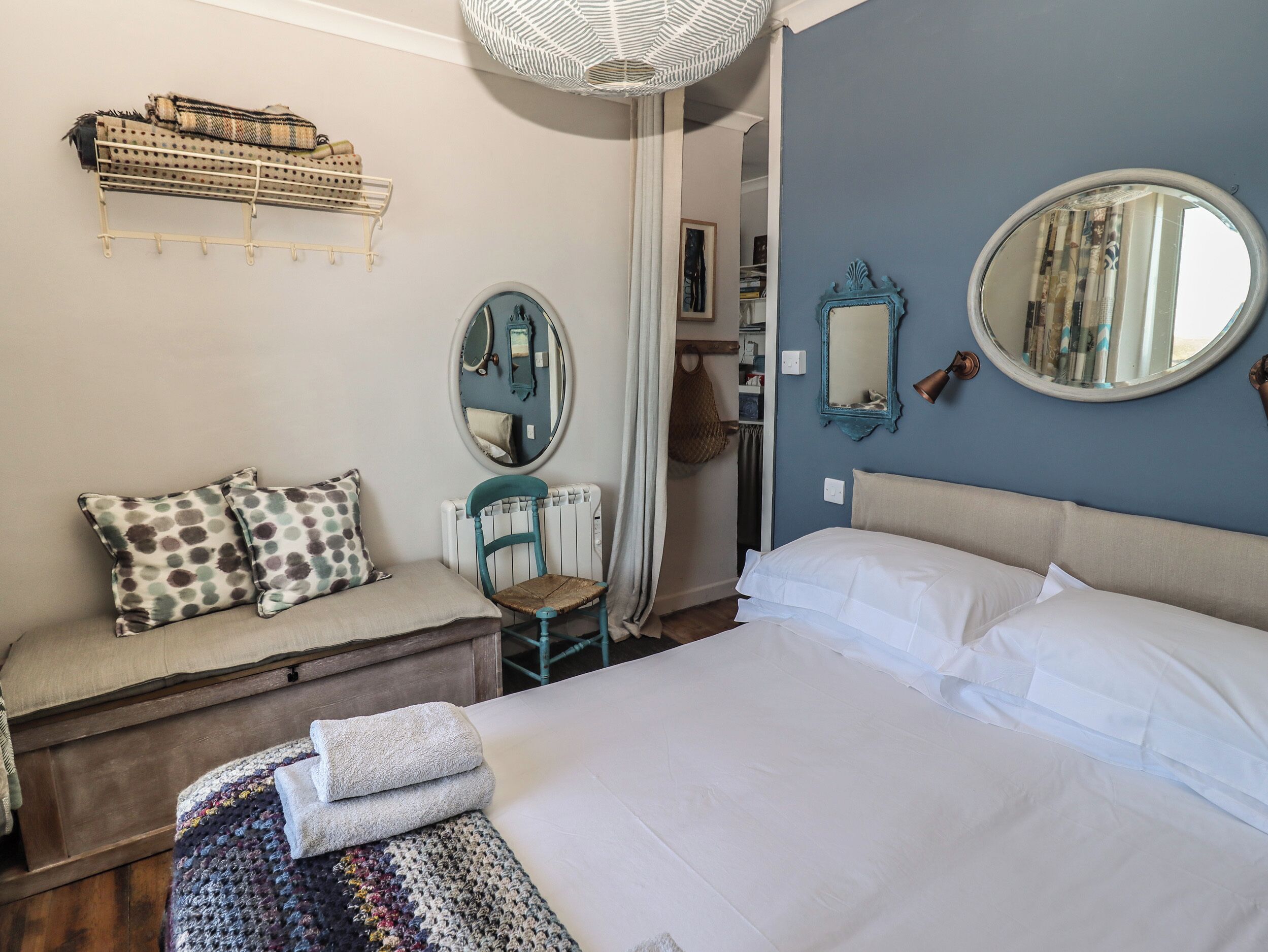 Une chambre à coucher comprenant un lit, une chaise, une petite table, un miroir et une étagère avec des serviettes.