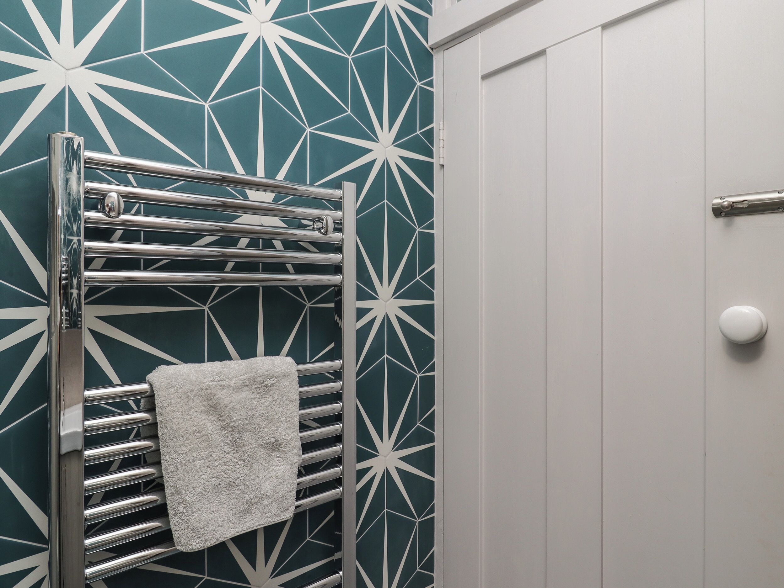 A bathroom with a towel rack holding a white towel, a door with a round handle, and a wall with a geometric pattern.