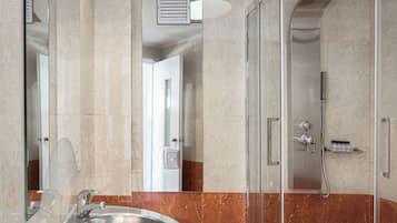A modern bathroom with a glass-enclosed shower, a marble-tiled floor, and a glass sink.